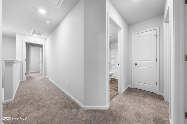 corridor featuring attic access, light colored carpet, visible vents, and baseboards