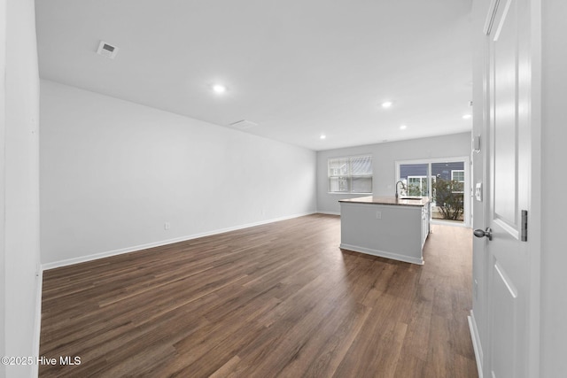 unfurnished living room with dark wood-style floors, recessed lighting, a sink, and baseboards