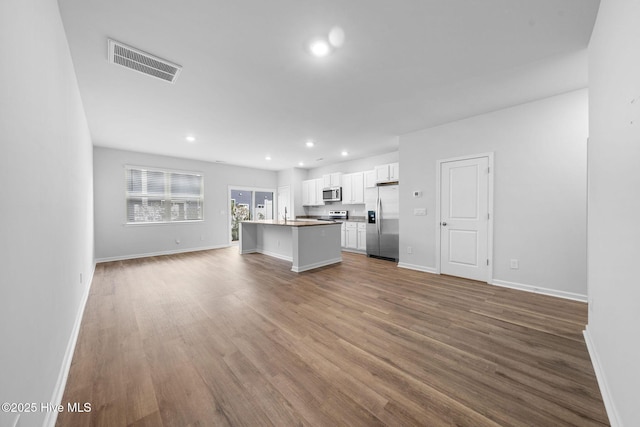 kitchen featuring a kitchen island with sink, stainless steel appliances, visible vents, white cabinets, and open floor plan