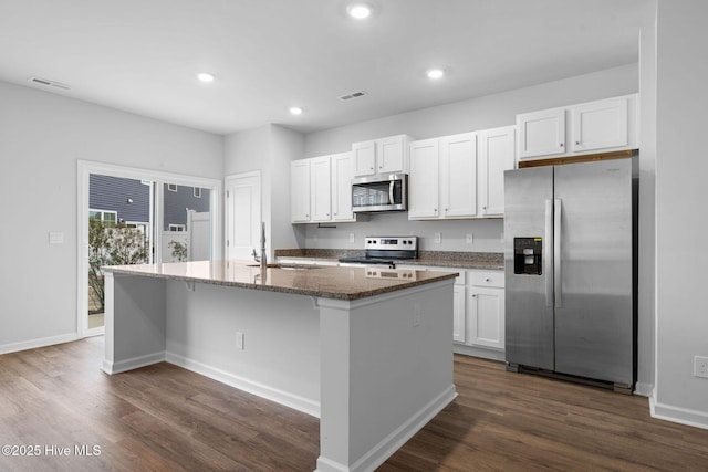 kitchen with a kitchen island with sink, stainless steel appliances, a sink, white cabinetry, and dark stone counters