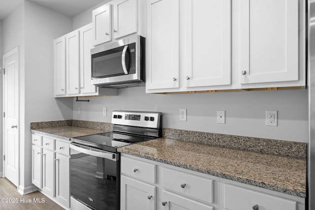 kitchen featuring stainless steel appliances, white cabinets, light wood finished floors, and dark stone countertops