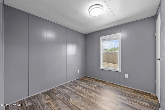 spare room with wood finished floors, a decorative wall, and a textured ceiling