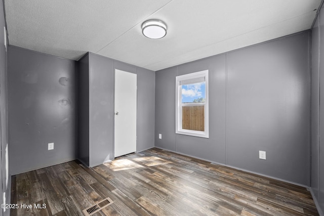 unfurnished room featuring wood finished floors, a textured ceiling, and visible vents