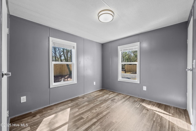 empty room with a textured ceiling, wood finished floors, and a healthy amount of sunlight
