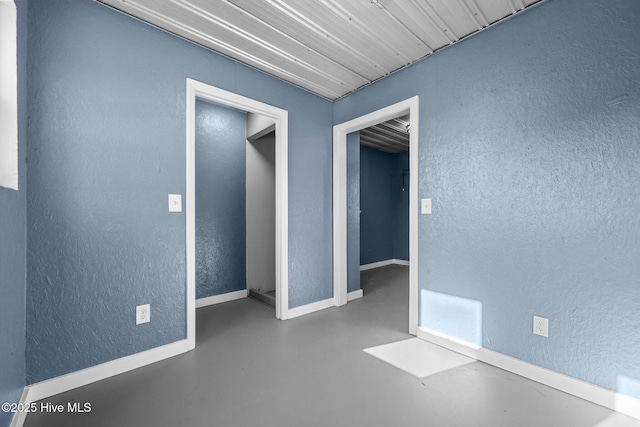 unfurnished room featuring finished concrete flooring, a textured wall, baseboards, and visible vents