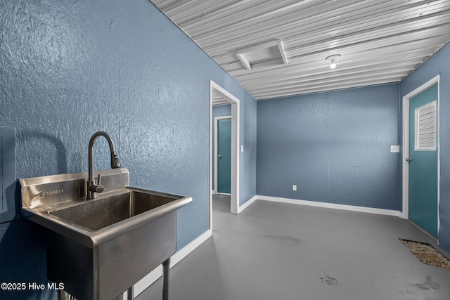 kitchen featuring a sink, a textured wall, baseboards, and concrete floors