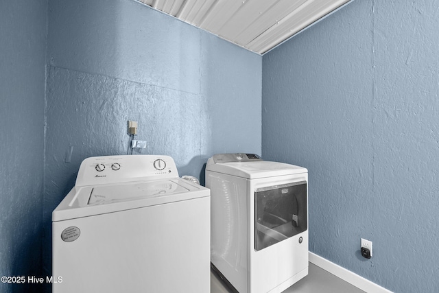 clothes washing area with baseboards, washing machine and dryer, laundry area, and a textured wall
