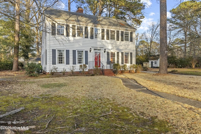 colonial house with a storage unit, an outdoor structure, a front lawn, and a chimney