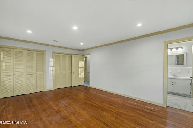 unfurnished bedroom featuring ornamental molding, wood finished floors, two closets, recessed lighting, and ensuite bath