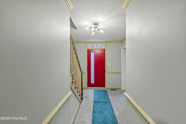 doorway with a notable chandelier, ornamental molding, and carpet floors