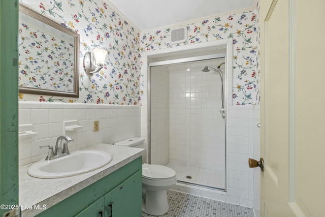 bathroom featuring toilet, wallpapered walls, a shower stall, and a wainscoted wall