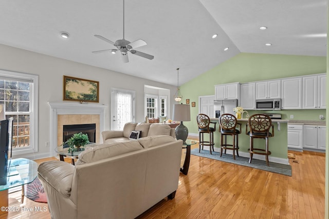 living room with a tile fireplace, light hardwood / wood-style floors, high vaulted ceiling, and ceiling fan