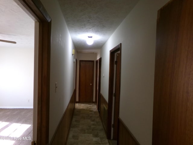 corridor with dark carpet, a textured ceiling, and baseboards