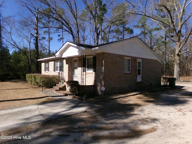 view of side of property with crawl space, brick siding, and driveway