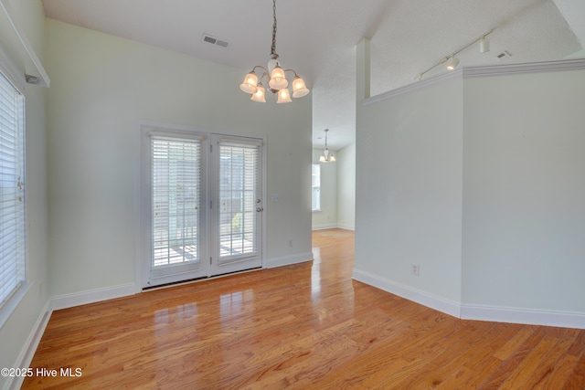 unfurnished dining area featuring baseboards, track lighting, light wood-style flooring, and an inviting chandelier