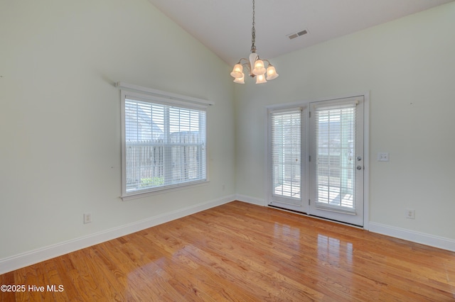 empty room featuring baseboards, visible vents, wood finished floors, vaulted ceiling, and a chandelier