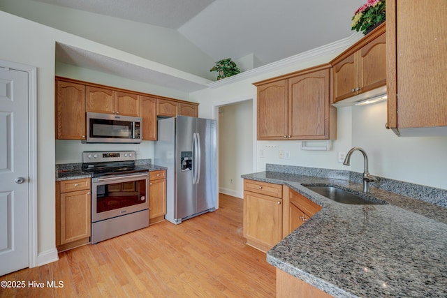 kitchen with light wood finished floors, stainless steel appliances, stone countertops, vaulted ceiling, and a sink