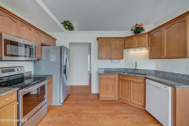 kitchen with a sink, appliances with stainless steel finishes, ornamental molding, light wood-type flooring, and dark stone counters