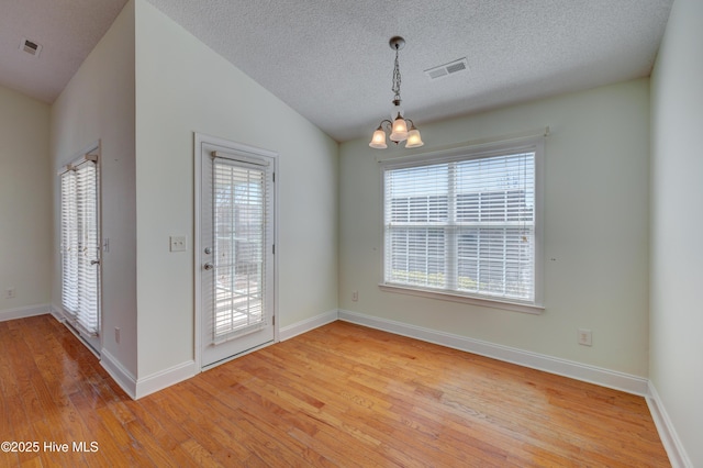 unfurnished dining area featuring lofted ceiling, visible vents, a notable chandelier, and light wood finished floors