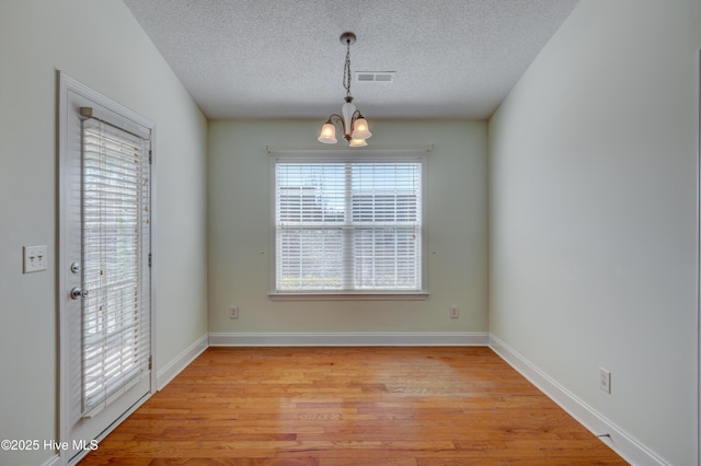 unfurnished dining area featuring light wood finished floors, visible vents, an inviting chandelier, a textured ceiling, and baseboards