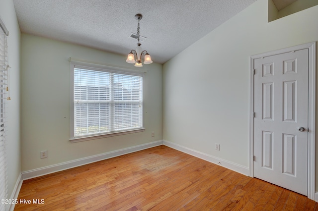 spare room featuring light wood finished floors, visible vents, a textured ceiling, a chandelier, and baseboards