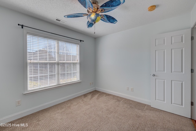 carpeted spare room with a textured ceiling, visible vents, a ceiling fan, and baseboards