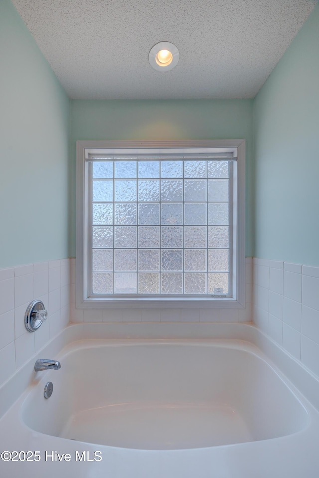 full bath with a garden tub and a textured ceiling