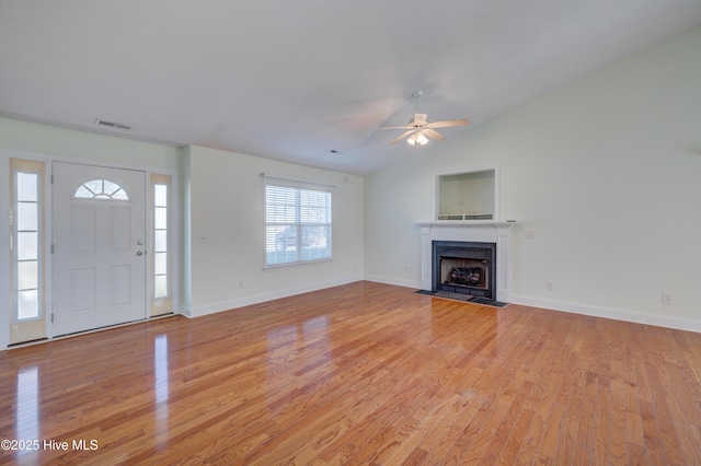 unfurnished living room featuring lofted ceiling, visible vents, a fireplace with flush hearth, light wood-style floors, and baseboards