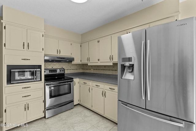 kitchen with cream cabinetry, stainless steel appliances, dark countertops, backsplash, and under cabinet range hood