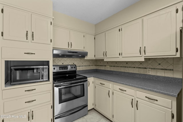 kitchen with stainless steel appliances, dark countertops, under cabinet range hood, and tasteful backsplash