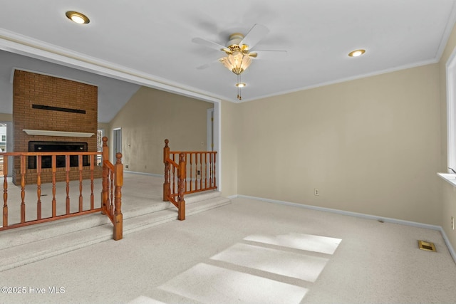 spare room with crown molding, a brick fireplace, carpet flooring, and baseboards