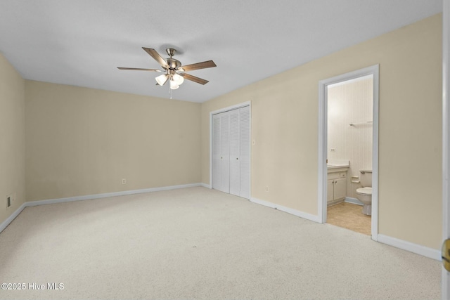 unfurnished bedroom featuring ceiling fan, light colored carpet, baseboards, a closet, and ensuite bath