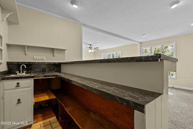 kitchen with a textured ceiling, light colored carpet, a sink, white cabinetry, and dark countertops