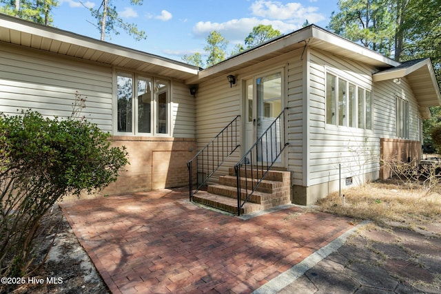 view of front facade with crawl space, entry steps, brick siding, and a patio