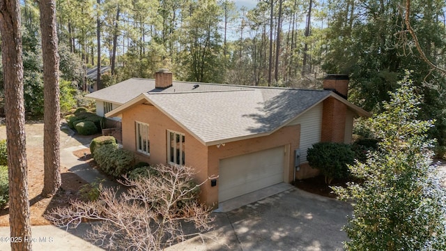 view of side of home with driveway, a garage, a chimney, and roof with shingles