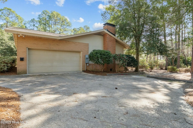 view of property exterior with a garage, brick siding, a chimney, and aphalt driveway