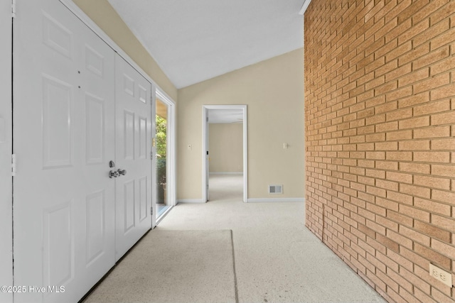 entrance foyer featuring lofted ceiling, light colored carpet, visible vents, brick wall, and baseboards