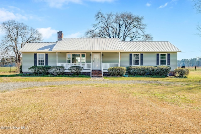 ranch-style home featuring metal roof, covered porch, a chimney, and a front lawn