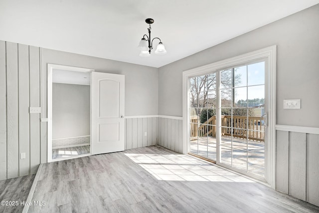 unfurnished dining area featuring a wainscoted wall, light wood finished floors, and a notable chandelier