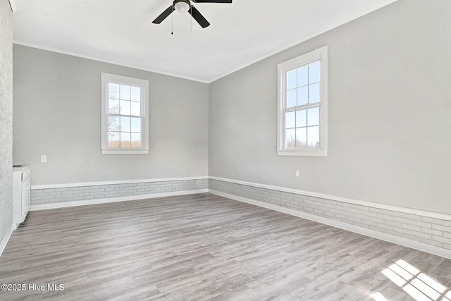 empty room with a healthy amount of sunlight, light wood finished floors, and brick wall