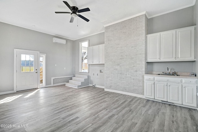 unfurnished living room with a wall unit AC, light wood finished floors, ornamental molding, and a sink