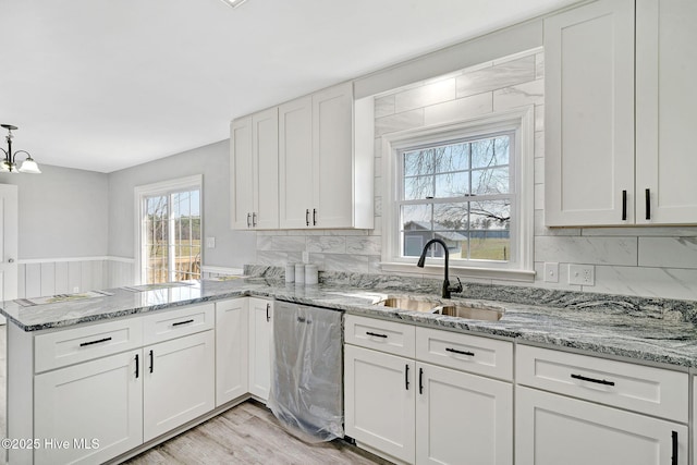 kitchen with dishwasher, decorative backsplash, a sink, and white cabinets