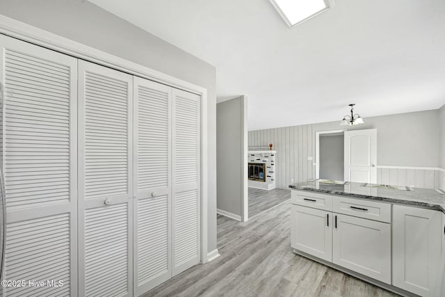 kitchen with pendant lighting, light wood-style flooring, white cabinets, dark stone counters, and baseboards