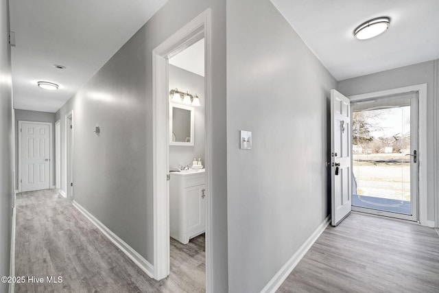 corridor with light wood finished floors, baseboards, and a sink
