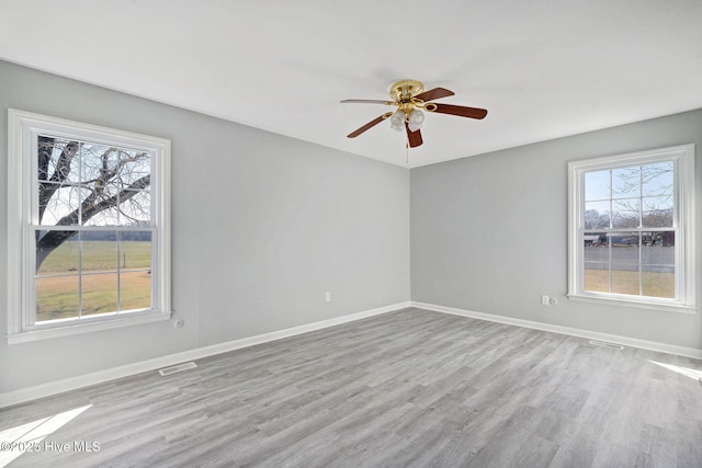 empty room featuring a ceiling fan, visible vents, light wood finished floors, and baseboards