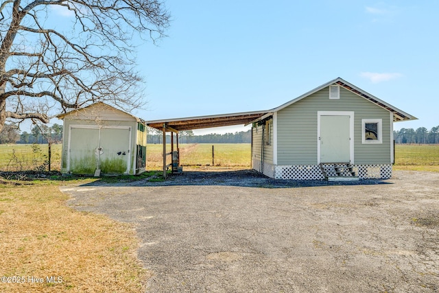 view of outdoor structure with an outbuilding, a carport, a rural view, and entry steps