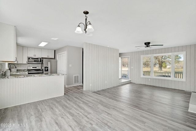 kitchen featuring a peninsula, white cabinetry, open floor plan, hanging light fixtures, and appliances with stainless steel finishes
