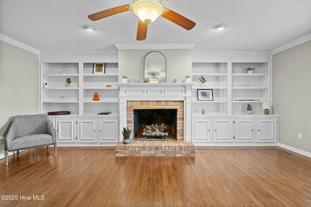 living area with a fireplace, built in features, baseboards, ornamental molding, and light wood-type flooring