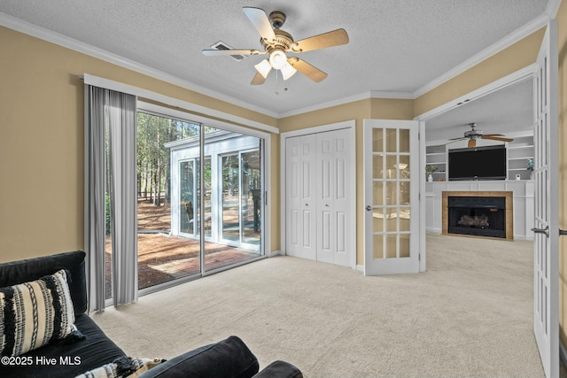 living area featuring ceiling fan, a textured ceiling, a tile fireplace, light carpet, and crown molding