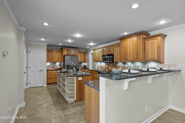 kitchen featuring brown cabinets, a center island with sink, appliances with stainless steel finishes, dark stone countertops, and a kitchen breakfast bar